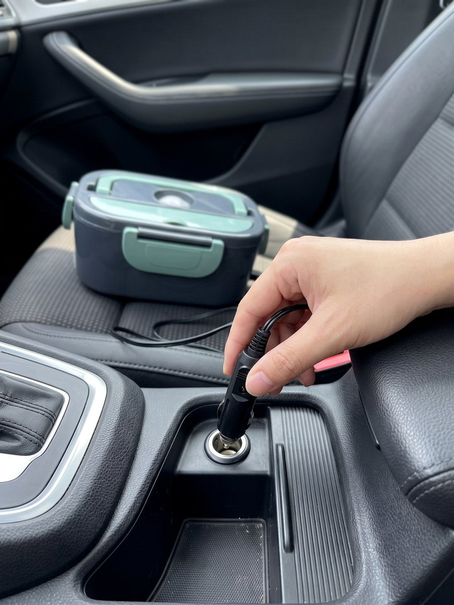 Hand steekt de autostekker in de 12V-aansluiting, de lunchbox staat op de stoel ernaast