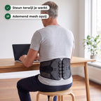 Man zit op een kruk achter zijn laptop met de rugbrace midden op zijn onderrug