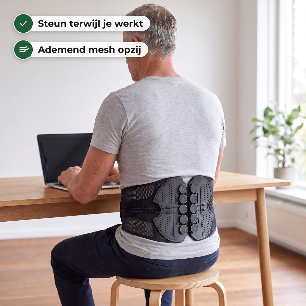 Man zit op een kruk achter zijn laptop met de rugbrace midden op zijn onderrug