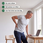 Man staat op van zijn bureau en houdt zijn hand op zijn onderrug