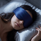 Vrouw slaapt op haar zij met het marineblauwe zijden slaapmasker op, dat doorloopt tot over haar slaap, met haar wang op een satijnen kussensloop