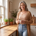 Vrouw in de keuken met koffie, in de beige comfort top onder een open camel vest en een spijkerbroek