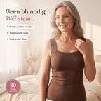 Lachende vrouw van rond de vijftig in de bruine comfort top met ingebouwde bh, hand aan het brede bandje, in een zonnige slaapkamer