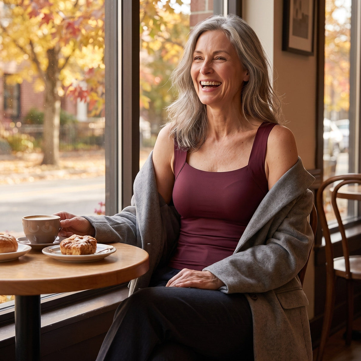 Lachende vrouw in een café in de wijnrode comfort top met een grijze blazer over haar schouders