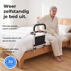Oudere vrouw zit op de rand van haar bed en duwt zich zelfstandig omhoog aan de schuimgreep van de bedbeugel