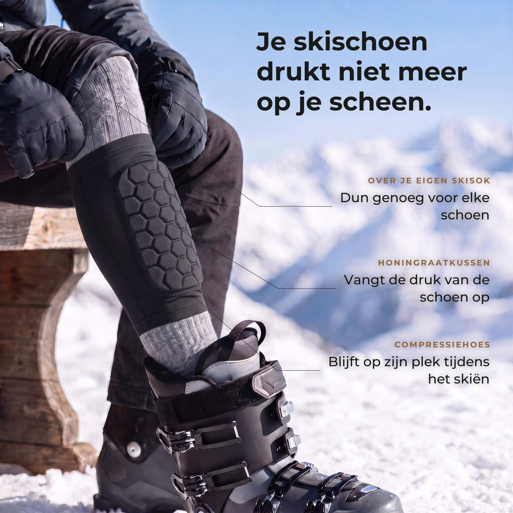 Skiër op een bank met de korte zwarte scheenbeschermer met honingraatkussen over de grijze skisok, voet in de skischoen, met drie uitleglabels