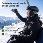 Skiër in de stoeltjeslift maakt een foto, zijn telefoon zit met een dun koord vast aan de koordrol op zijn rugzakband