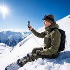 Snowboarder zit in de sneeuw boven een steile helling en filmt het uitzicht, telefoon aan het koord