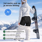 Snowboardster op de piste trekt haar witte skibroek iets omlaag en laat de zwarte valschort met stuitschild en heuppads zien, met drie uitleglabels en een zegel 30 dagen niet goed geld terug