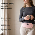 Vrouw met een mok thee draagt de roze draadloze warmteband om haar onderbuik over een grijs shirt