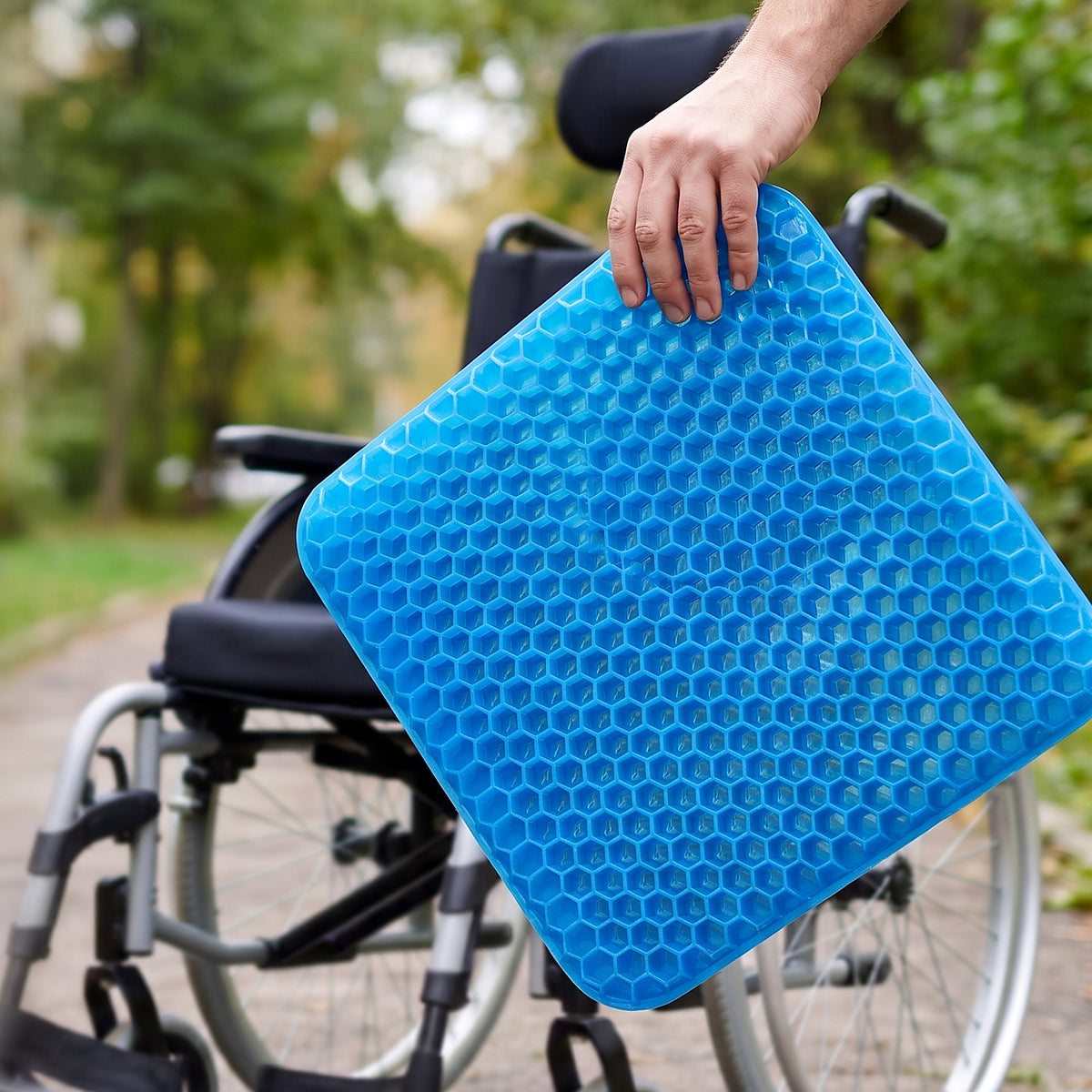 Hand houdt het blauwe honingraat zitkussen omhoog naast een rolstoel, van dichtbij zodat de honingraatcellen goed te zien zijn