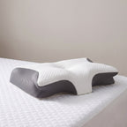 Het vlinderkussen op de hoek van een bed met een wit gewatteerd matrasbeschermer tegen een lichtgrijze muur