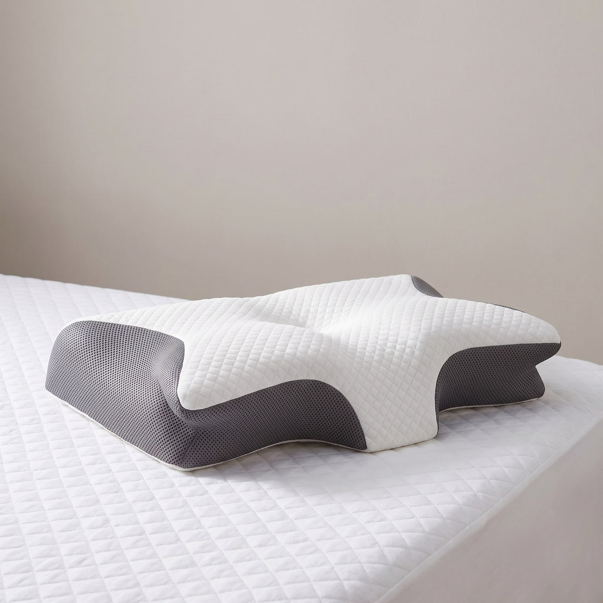 Het vlinderkussen op de hoek van een bed met een wit gewatteerd matrasbeschermer tegen een lichtgrijze muur