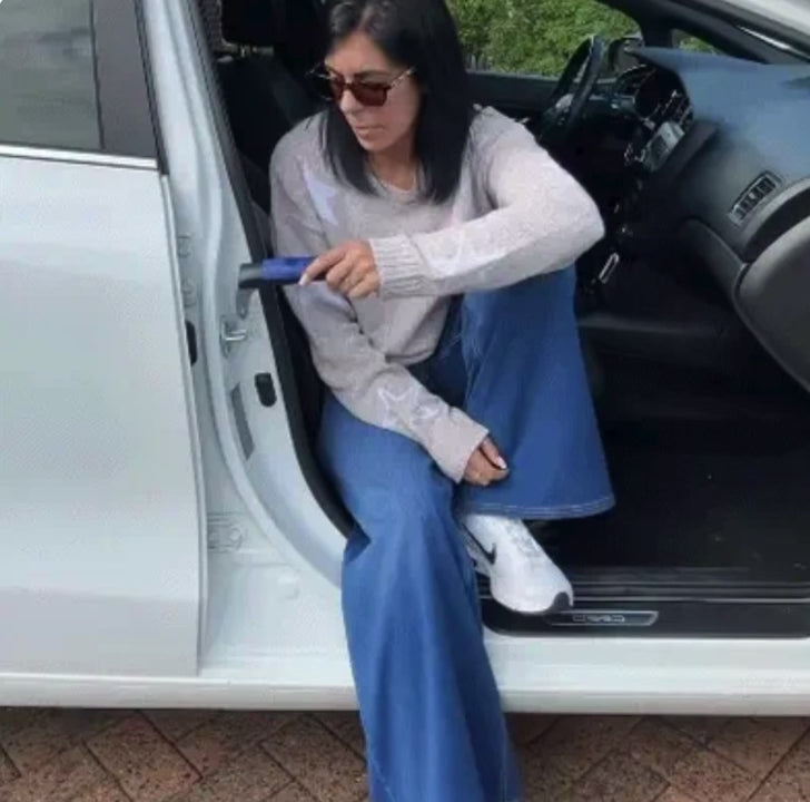 Vrouw stapt uit een witte auto terwijl ze zich vasthoudt aan de steungreep in de deurstijl