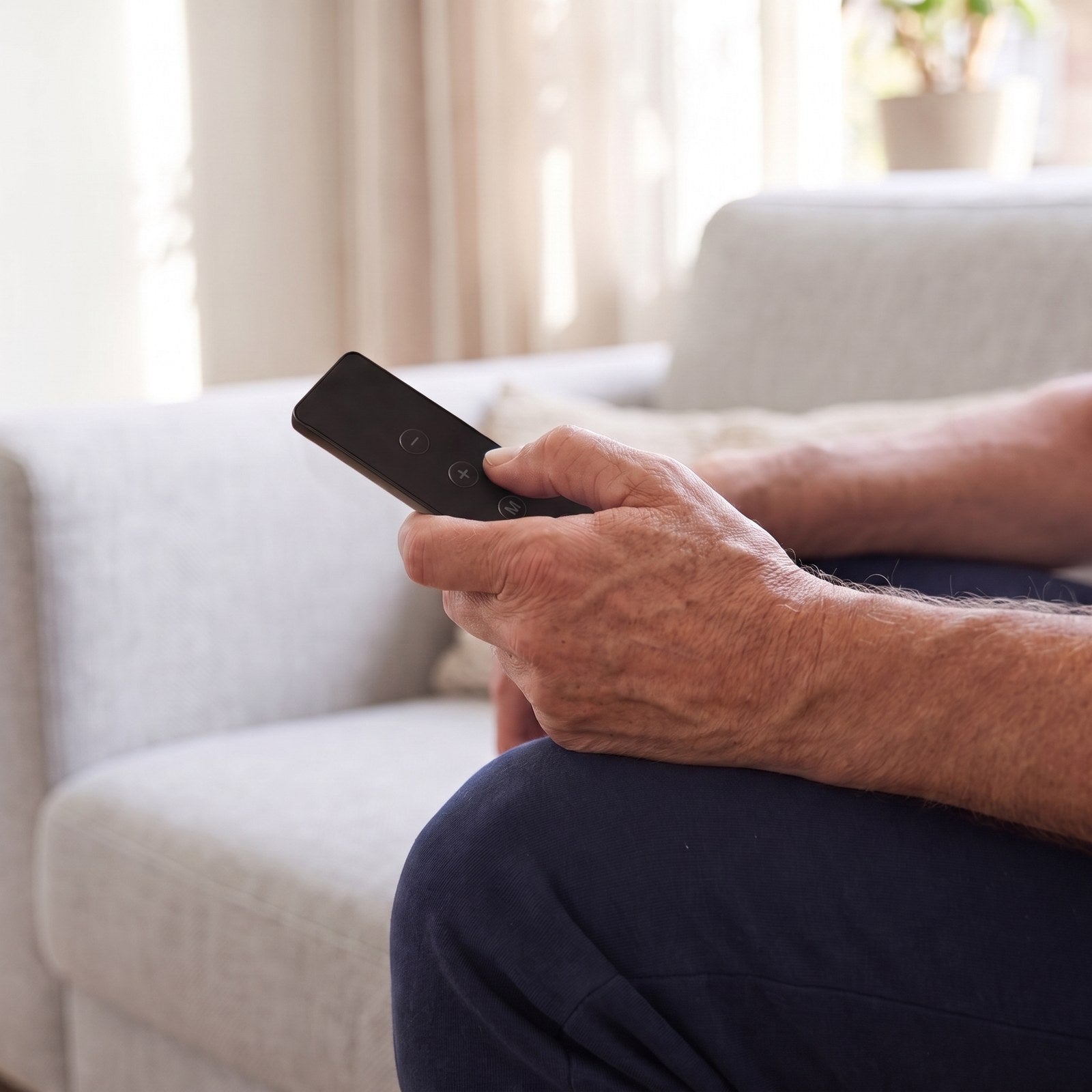 Hand op een knie met de zwarte afstandsbediening, duim op de plusknop
