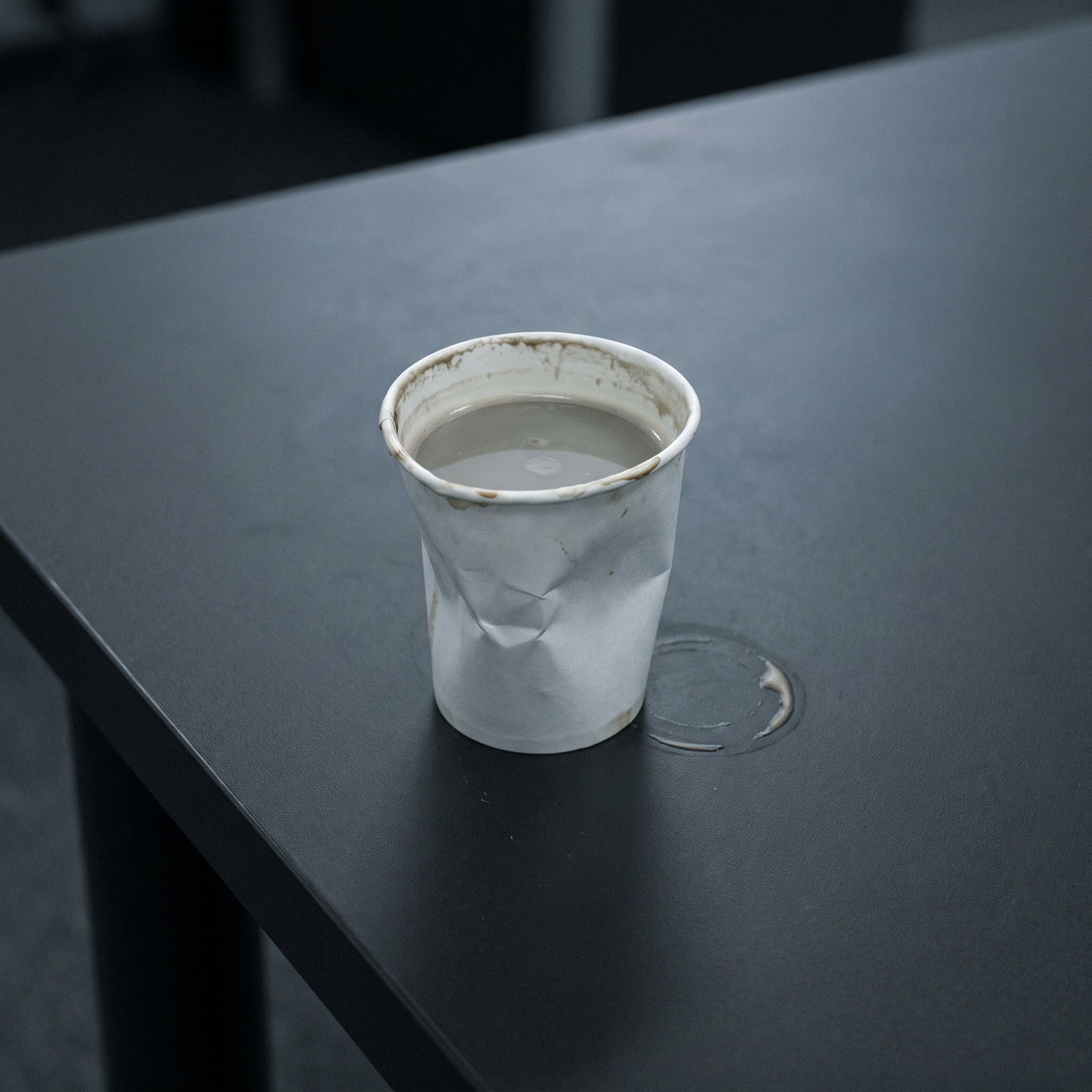 Verkreukeld wit bekertje met bleke, dunne automatenkoffie op een donker blad