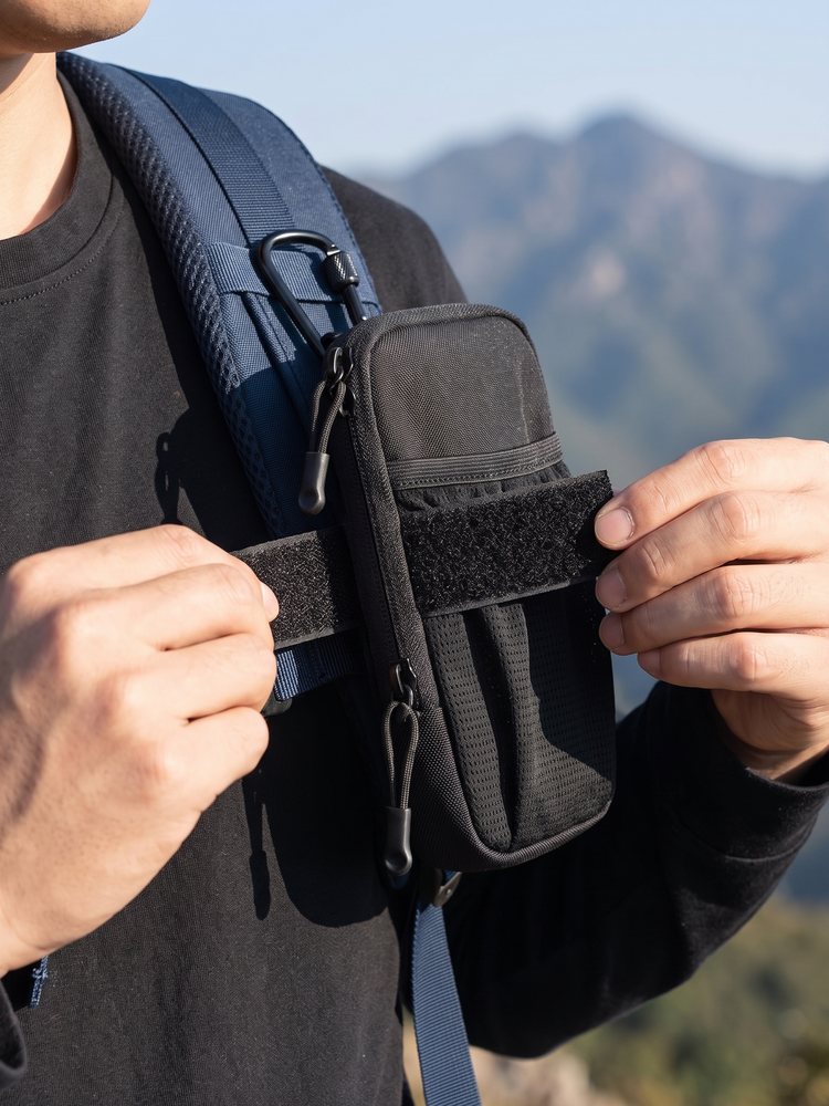 Handen zetten het zwarte telefoontasje met klittenband vast op een rugzakband