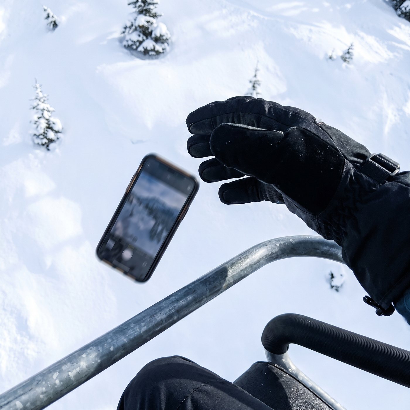 Telefoon glipt uit een skihandschoen boven de leegte onder een stoeltjeslift